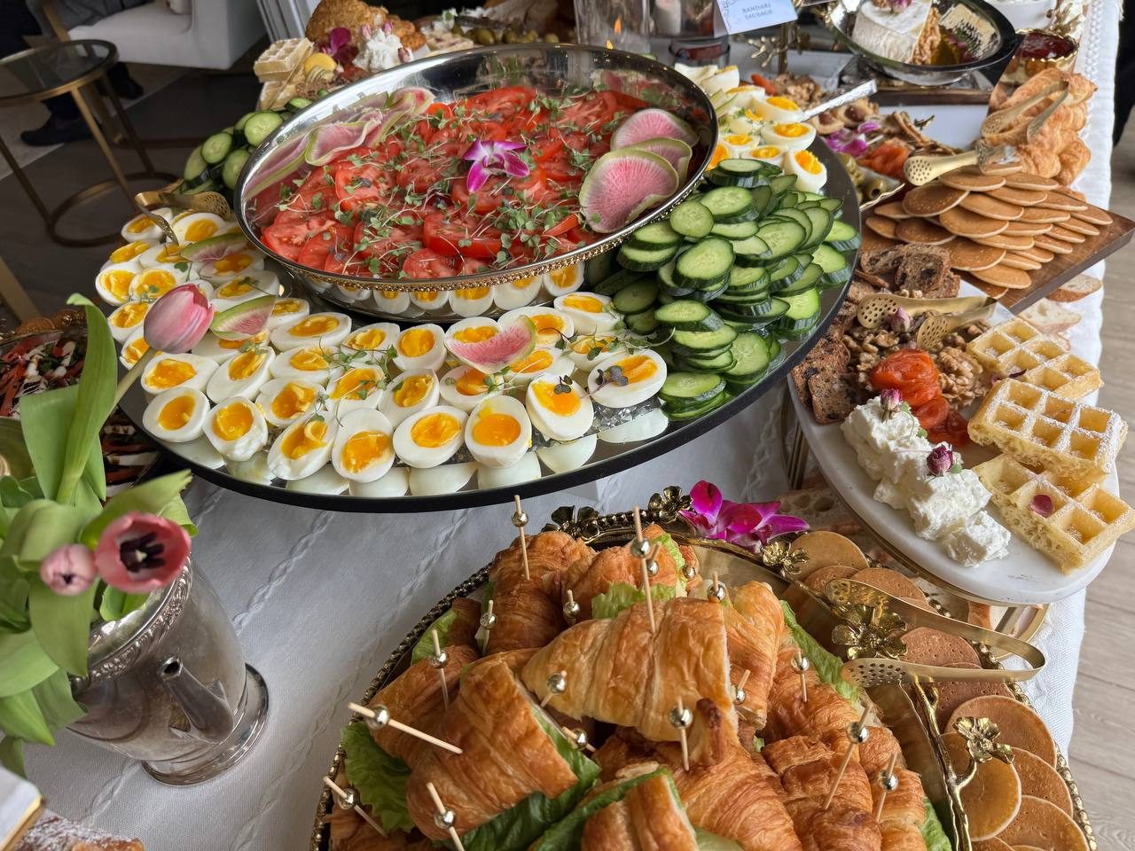 Brunch platters of eggs, cucumber, tomato, croissant sandwiches and waffles