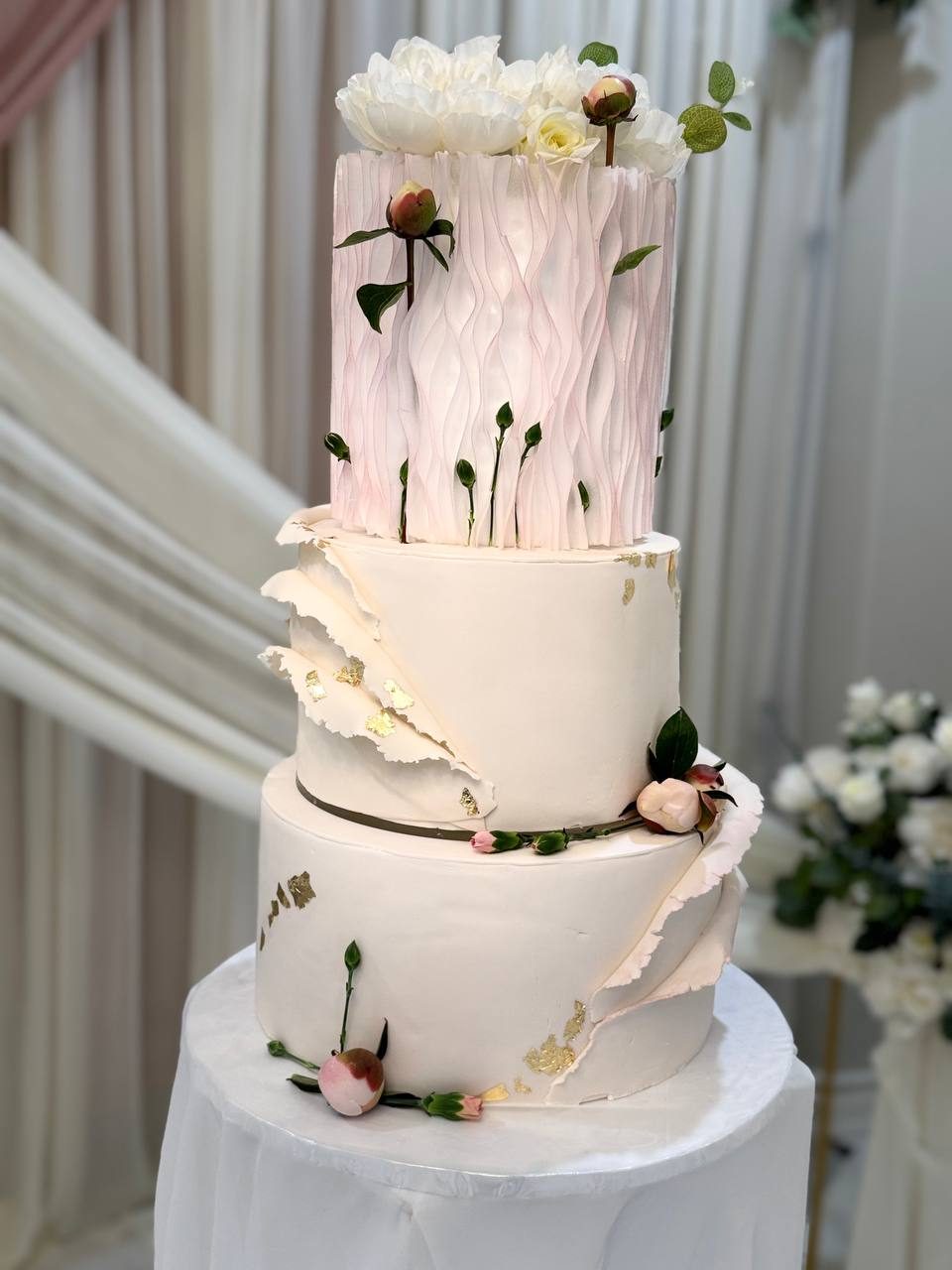 Three-tier wedding cake with sculpted white fondant and peonies
