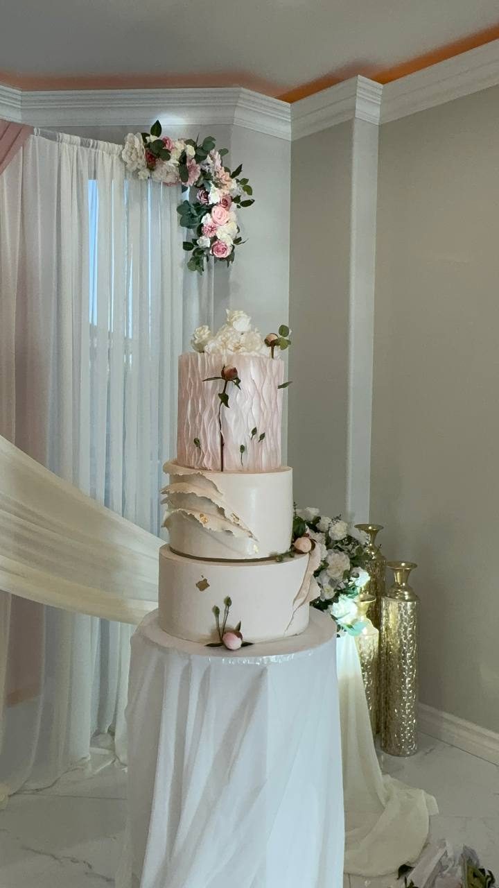Tall wedding cake beside a draped archway with florals