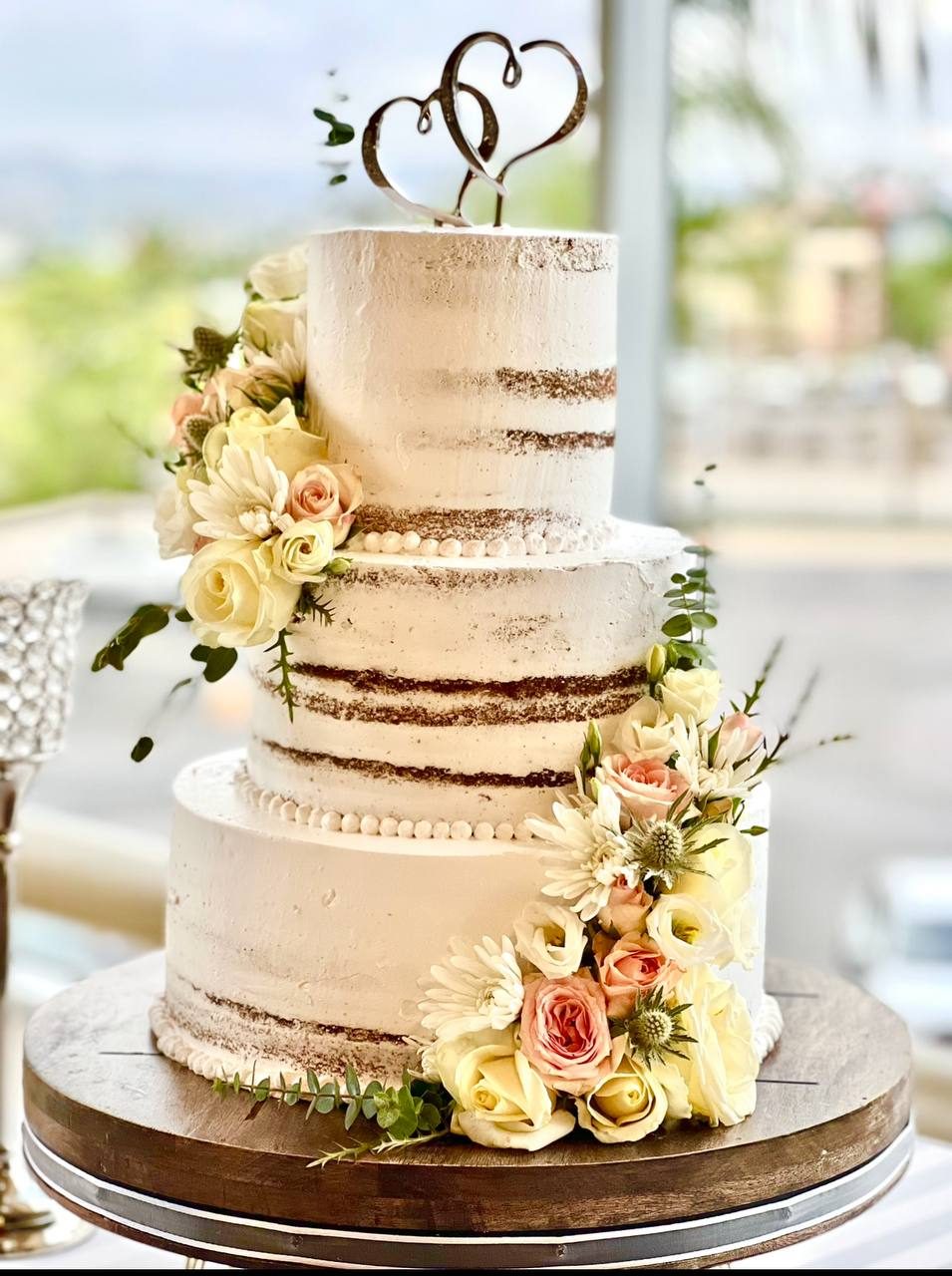 Semi-naked wedding cake with fresh flowers and a heart topper