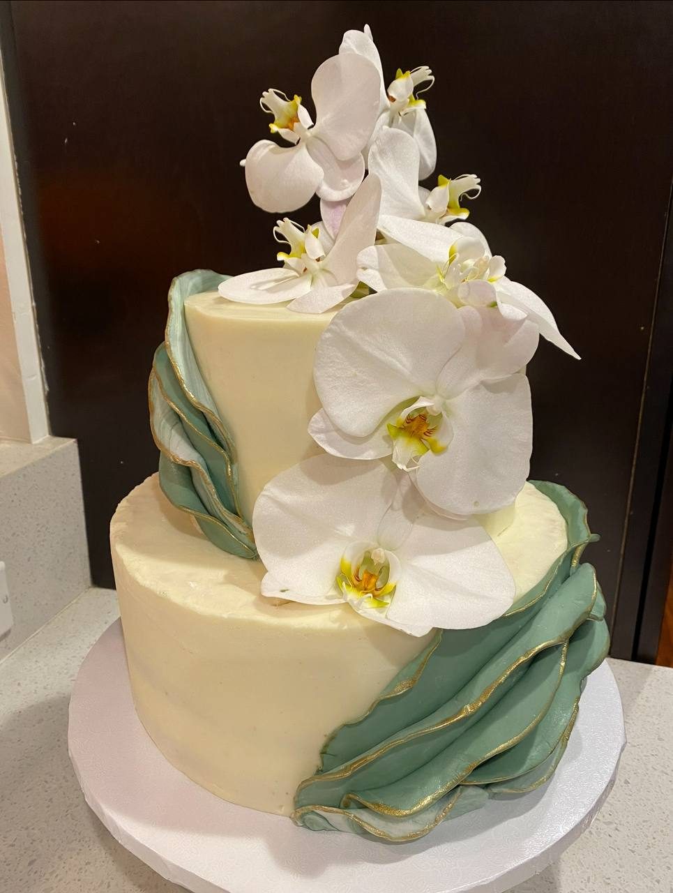 Two-tier wedding cake with white orchids and sage ribbon fondant