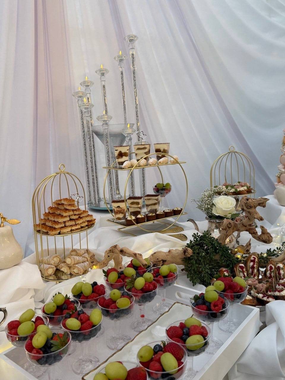 Dessert display with bird-cage stands, pastries, tiramisu cups and fruit